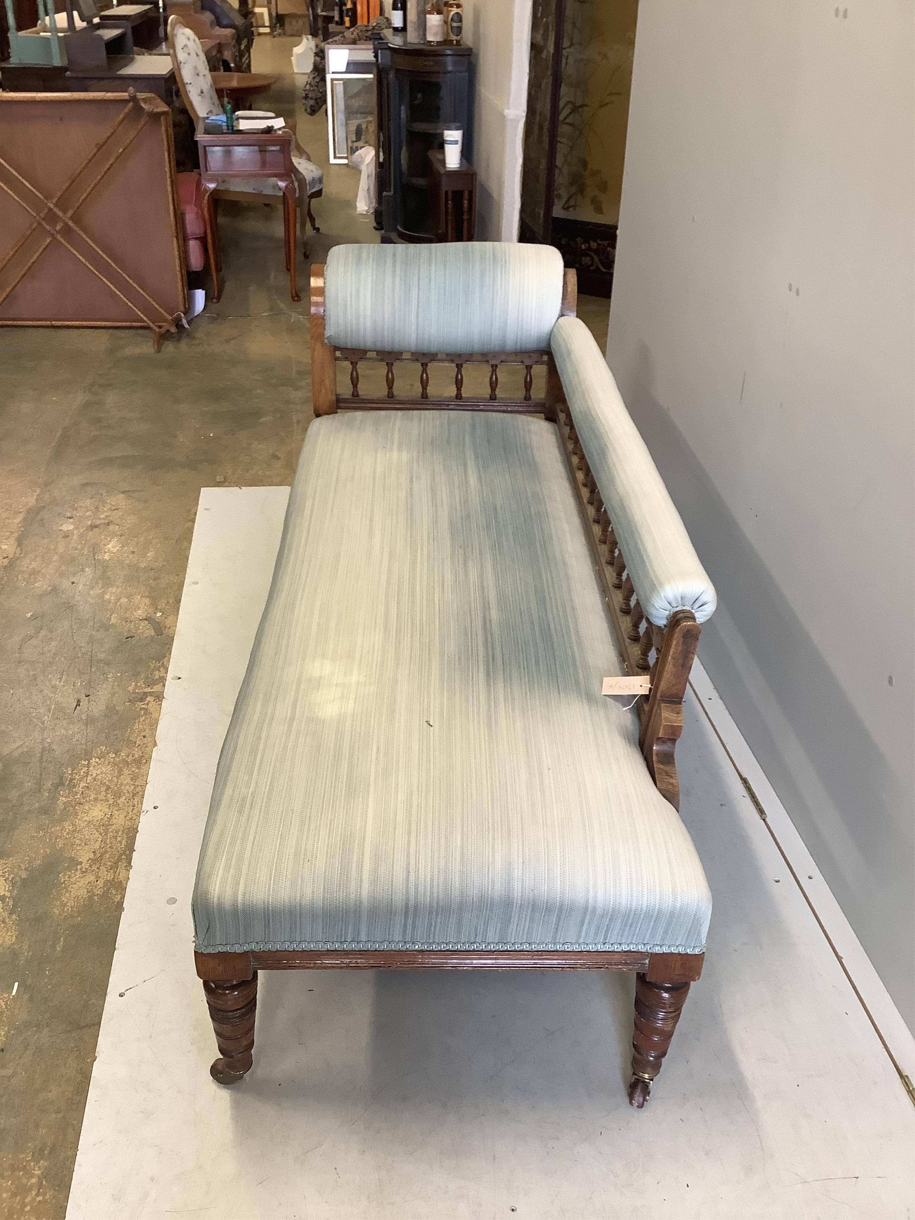 An Edwardian oak chaise longue, upholstered in green cord, on turned and carved legs fitted castors, width 184cm, depth 70cm, height 78cm. Condition - fair